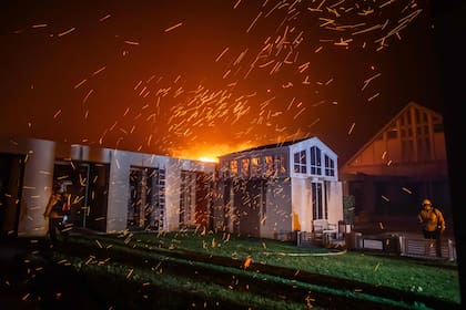 Los bomberos intentan que el fuego no alcance una vivienda amenazada por las llamas