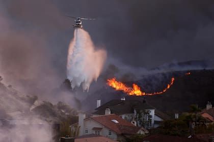 Un helicóptero arroja agua sobre las casas amenazadas por el incendio impulsado por el viento, en Pacific Palisades