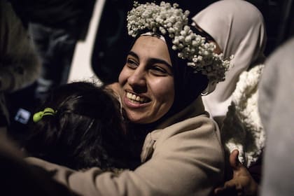 Una prisionera palestina, que lleva una corona de flores que recibió sobre su pañuelo, abraza a un pariente joven tras la llegada de unos 90 prisioneros liberados por Israel